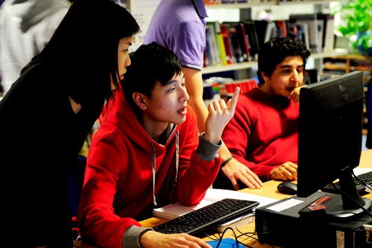 International student at INTO Manchester points up with one hand and holds computer mouse with other while looking at screen and listening to instructor. 