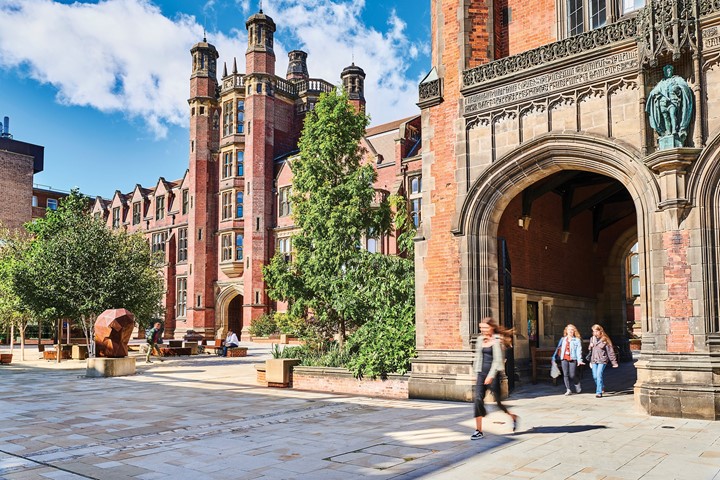 Students walk through ornate, brick arches at Newcastle University on a sunny day, with trees and sculpture in background.