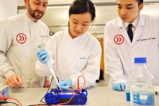INTO University of East Anglia international students conduct experiment involving electronic wires, wear latex gloves and INTO-branded white coats. 