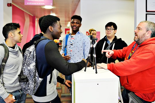 International students speak with instructor at desk with tripod in INTO Manchester Centre.