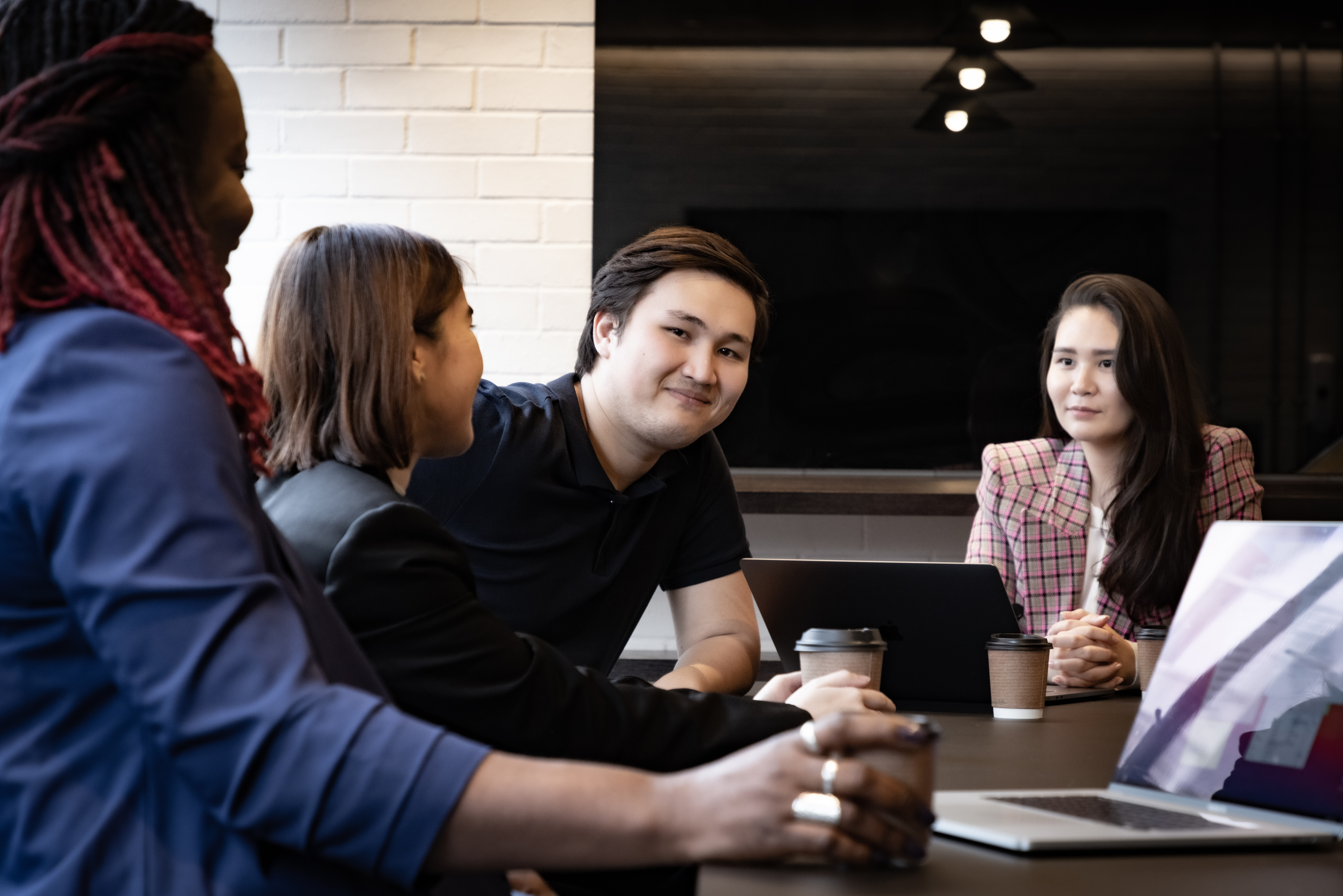 Four international graduates collaborate over desk, laptops and coffee.