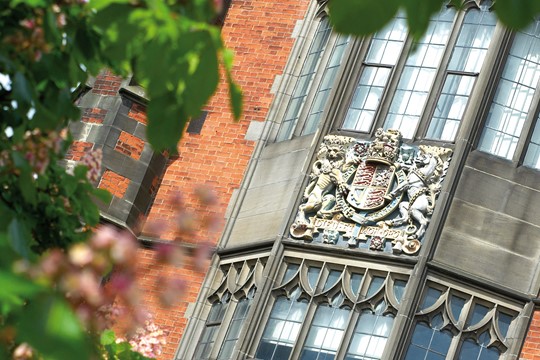 Ornate crest featuring horse and lion carved between two windows on brick building on Newcastle University campus.