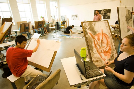 Visual arts class inside Drew University studio, with students working on canvases in semicircle. 