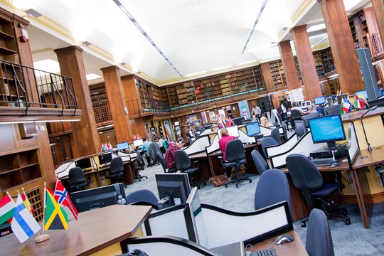 Interior of Newcastle University library, with rows of books on level two and students working at computer desks on level one. 