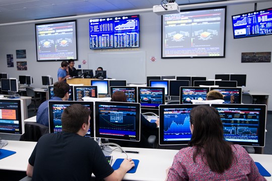 INTO Hofstra University instructor lectures international students about finance while students work at Bloomberg Terminals in Zarb School of Business.