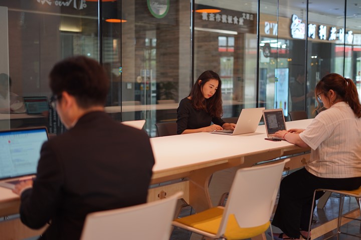 Prospective international students and education advisers work independently on laptops at long desk with yellow-seated chairs at INTO University Access Center in Suzhou, China.