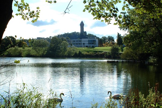 University of Stirling campus building with Wallace Monument tower in distance and pond with two swans in foreground.