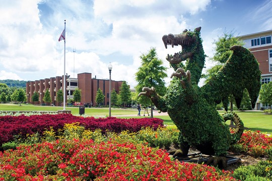 Statue of the UAB Blazer covered in ivy and set in bright, red bushes on the University of Alabama at Birmingham campus.