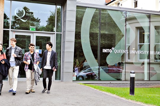 International students walk out of INTO Queen’s University Belfast Centre, holding coffee cups next to window displaying INTO roundel decal. 