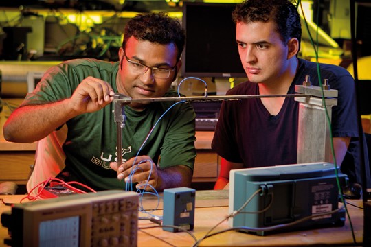 Two international students at INTO University of South Florida conduct experiment involving metal and electric wires in darkened laboratory.