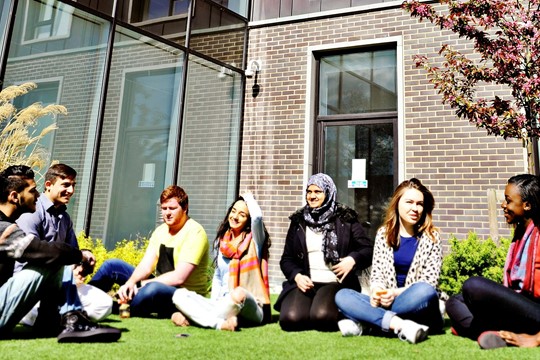 INTO London World Education Centre international students sit on green lawn adjacent to centre building.