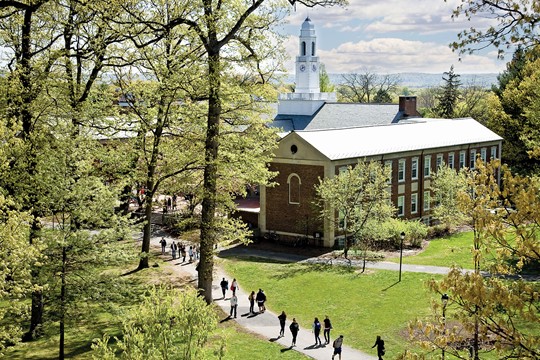 Exterior view of Brothers College Building on Drew University campus, with students walking down pathway and bright green trees in foreground.