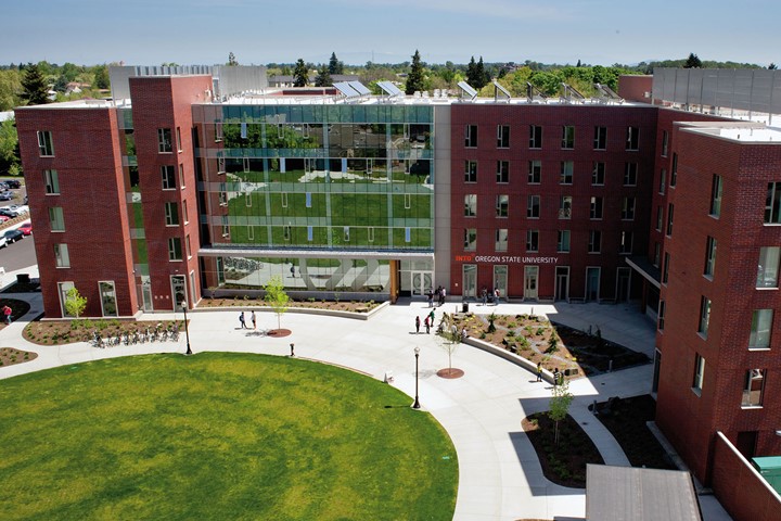 Five-story INTO Oregon State University International Living and Learning Center in heart of campus on sunny day, behind quad filled with students.