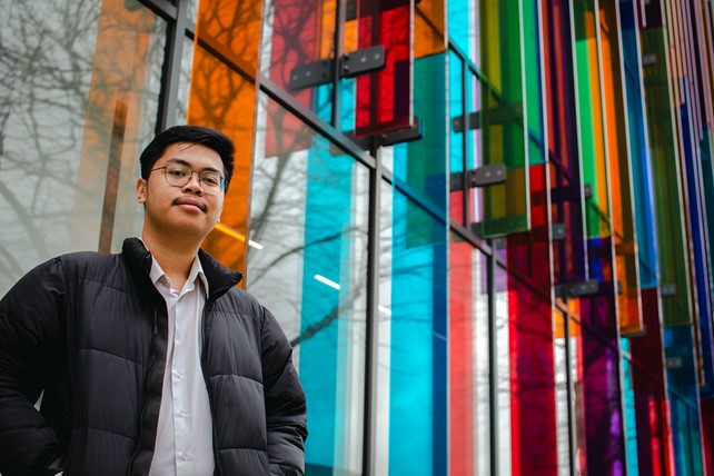 Queen's University Belfast student and INTO Queen's alumnus Daffa from Indonesia poses in front of a colorful building on campus.