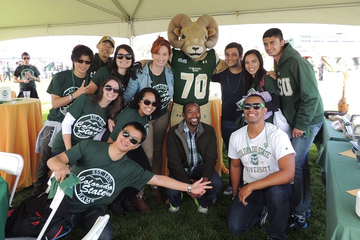 Eleven international students from INTO Colorado State University pose for picture with CSU mascot, the Ram, underneath tent at sporting event on bright day.