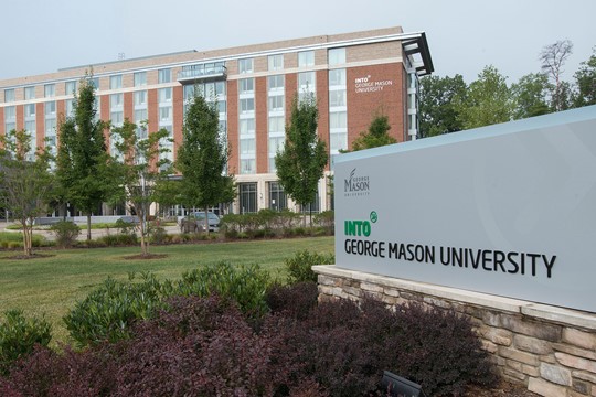Exterior view of seven-story, brick INTO George Mason University Center, with lawn, trees, and center sign in foreground.