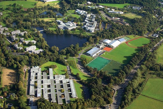 Aerial view of verdant University of Stirling campus, including sports fields and massive pond.