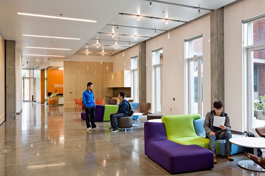 Communal area of INTO Oregon State University Living and Learning Center, with students conversing and reading on colorful couches near round tables.