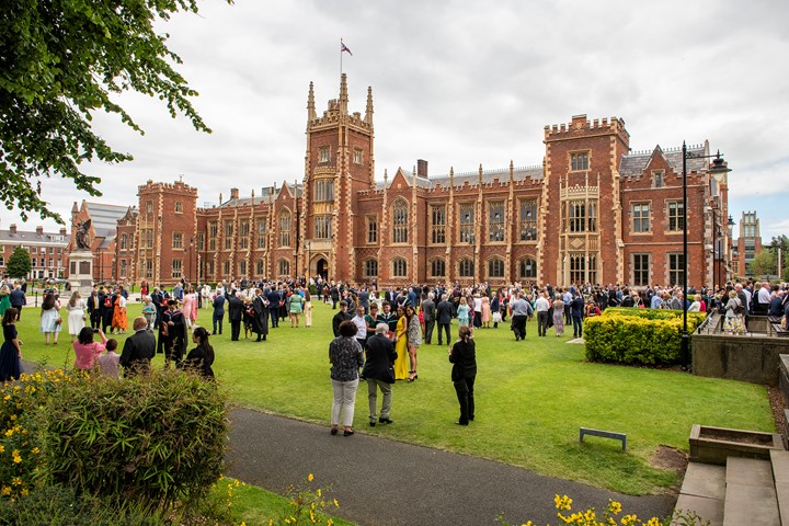 Students and parents gather on green lawn in front of Lanyon Building at Queen’s University Belfast for graduation ceremony on cloudy day.