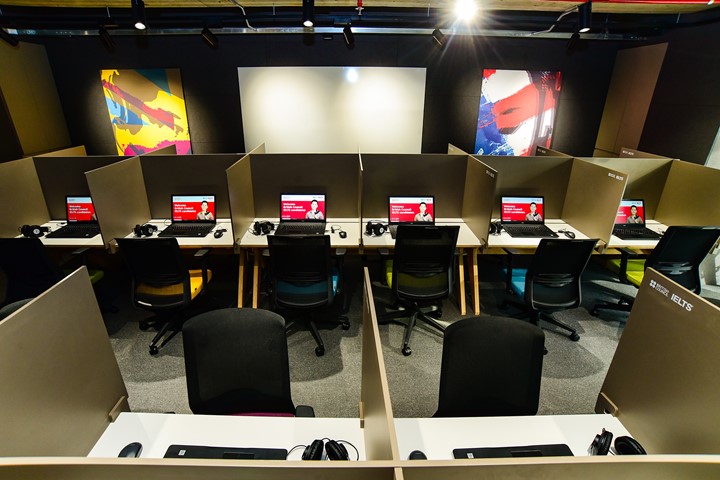Rows of booths with rolling chairs, laptops, and headphones where students take Computer-Delivered International English Language Testing System (IELTS CDI) and other exams, administered in partnership with British Council at INTO University Access Center in Ho Chi Minh City, Vietnam.