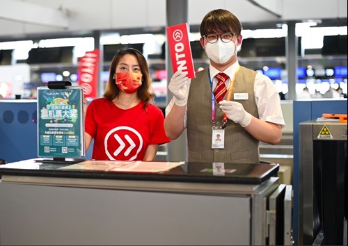 INTO staff member poses with Hong Kong airport agent while holding ticketholders featuring INTO logo.