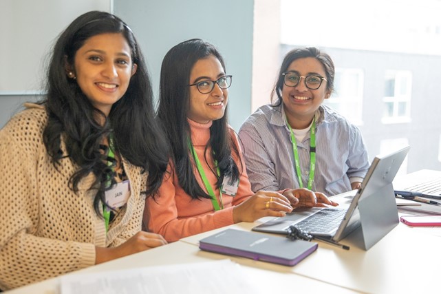 Three international students collaborate on data analysis project over laptop during INTO Summer Employment Boost program in London.
