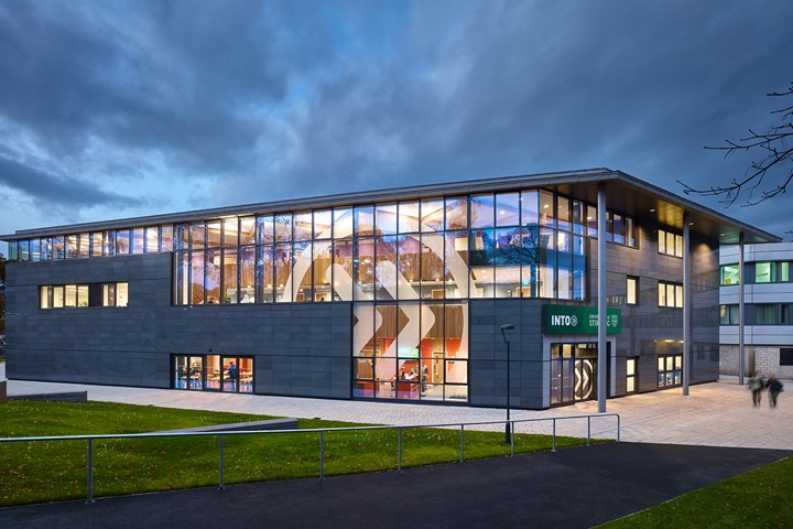 Exterior view of INTO University of Stirling Building at dusk, with many windows illuminated to display INTO roundel decal and students working inside.