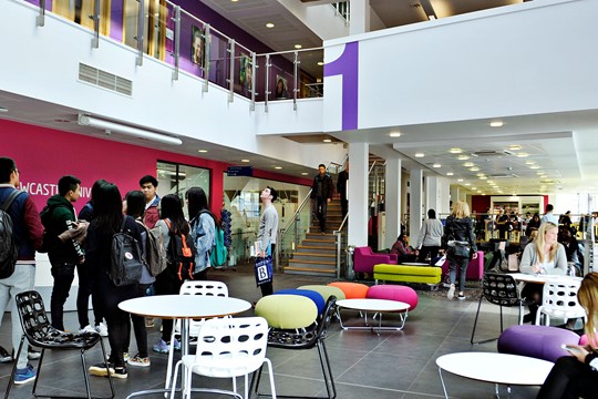 International students congregate in communal area of INTO Newcastle University Centre, surrounded by neon-colored furniture.