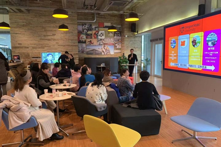 Educational advisor gives presentation on Oregon State Univesrtiy to group of prospective international students and parents seated on colorful chairs at round tables in INTO University Access Center in Suzhou, China.