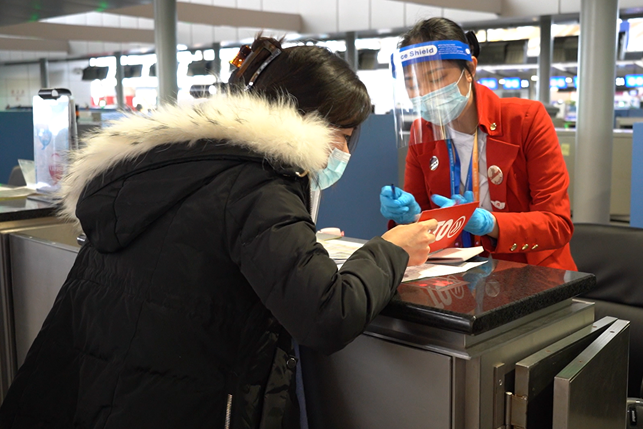 INTO student wearing face mask consults airport agent on flight information in advance of travel to UK at Shanghai Pudong airport.