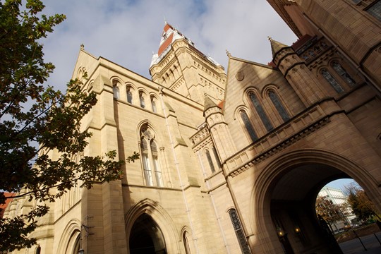 Angled view of The University of Manchester Arch shadowed by a stone building on campus.